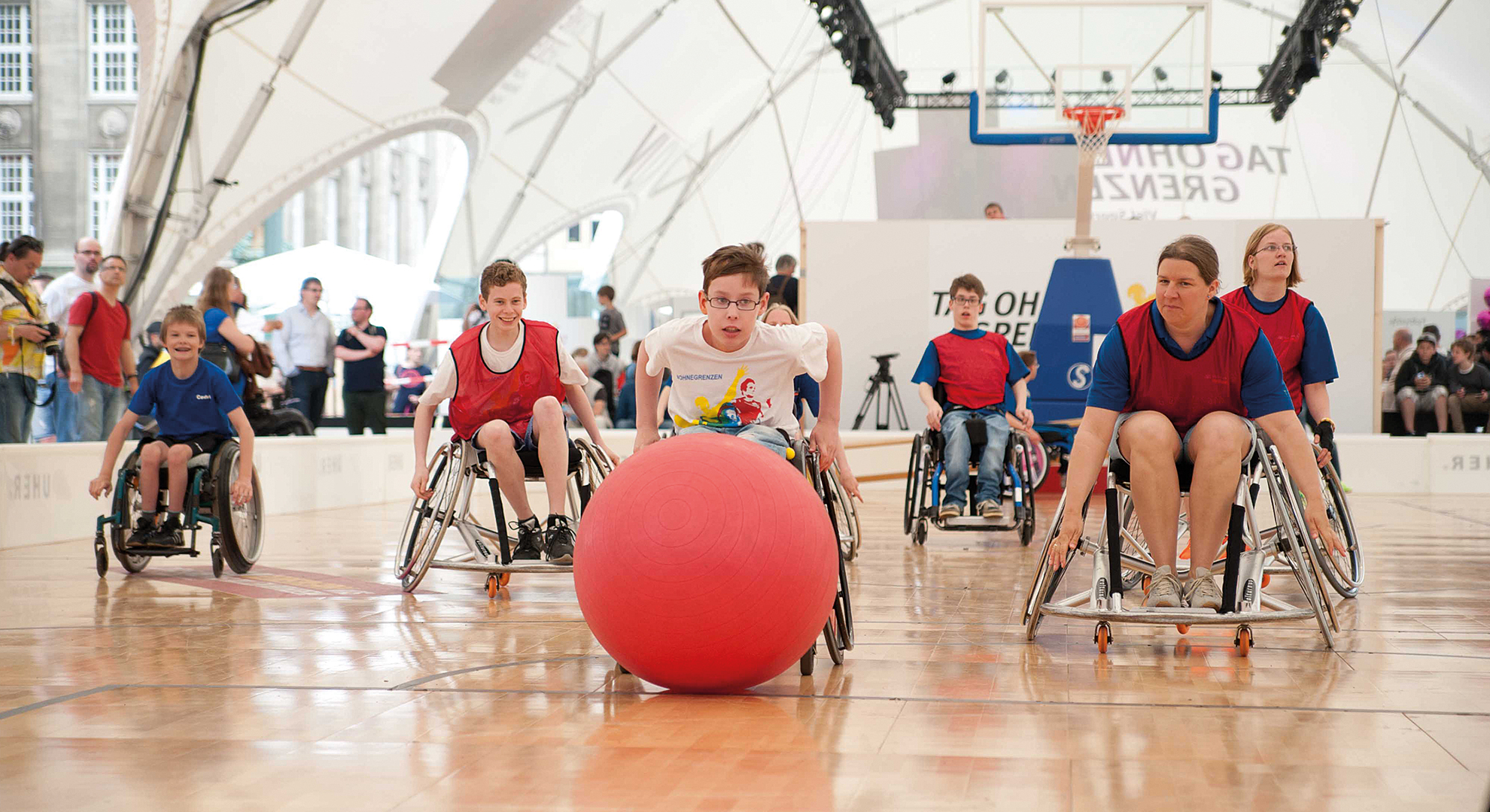 Jugendliche im Rollstuhl spielen mit einem großen Pezziball Wheel Soccer.